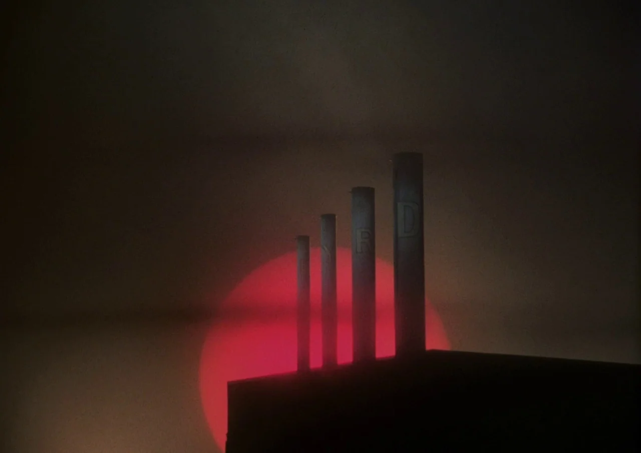 Human Highway (1982) movie still: establishing — Four vertical chimney stacks are arranged in a row atop a dark building. A large, circular glowing…