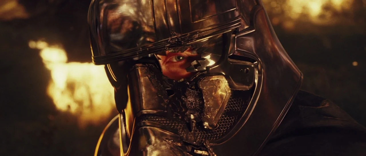 Star Wars: The Last Jedi (2017) movie still: closeup — A dark environment with glowing orange flames reflects off a damaged metallic helmet visor.…
