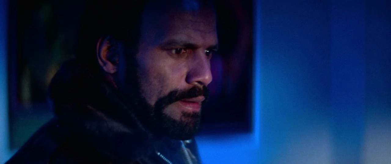 Vigilante (1982) movie still: closeup — An interior space is dimly lit by cool blue light emanating from one side. A middle-aged man with a beard…