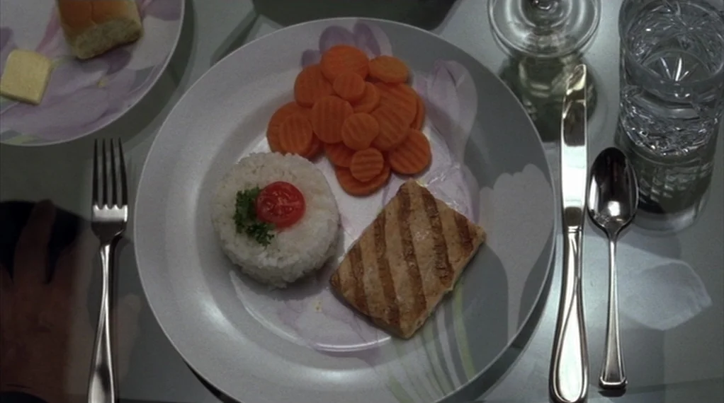 Broken Flowers movie still: closeup — A dinner plate with grilled fish, sliced carrots, and a mound of white rice. The table surface is glass and…