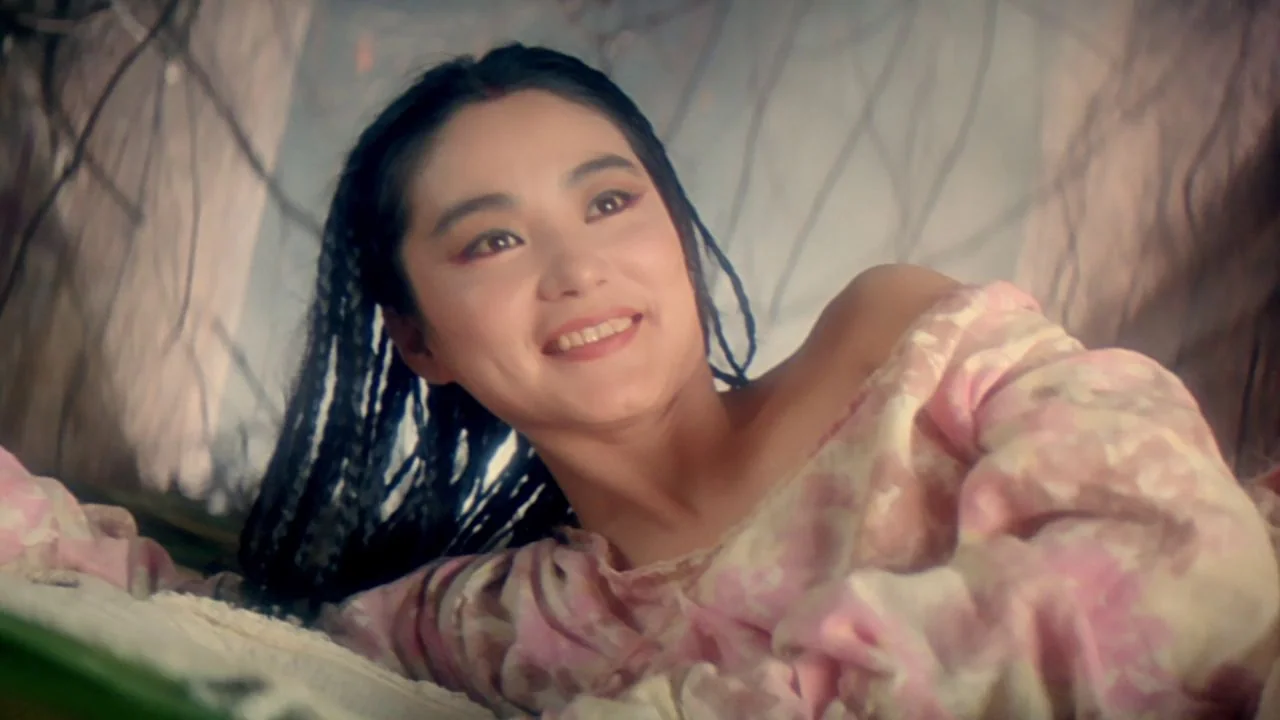 The Bride with White Hair II (1993) movie still: closeup — A woman lies on a surface surrounded by thin, blurred branches in a haze. She rests her…