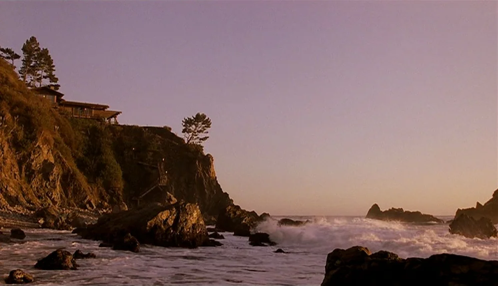 The Limey (1999) movie still: establishing — A rugged rocky coastline features a house perched on a high cliff edge. White foamy ocean waves wash…