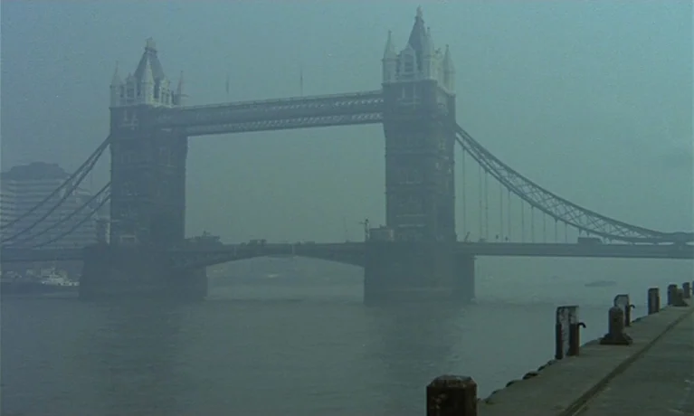 Nuits Rouges (1974) movie still: establishing — Tower Bridge in London rises out of heavy fog above the River Thames. A concrete dock with metal…