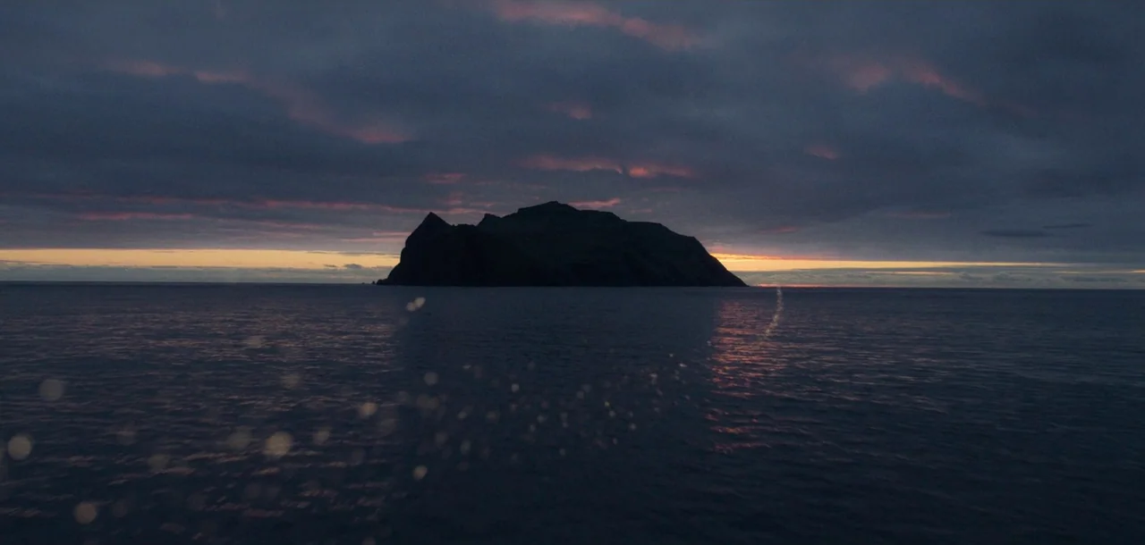 Peter Pan & Wendy (2023) movie still: establishing — A dark rocky island rises from a vast expanse of calm ocean water. The twilight sky above is…