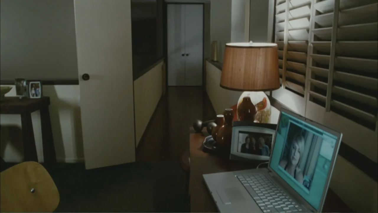 The Stepfather (2009) movie still: medium — An interior space features a desk with a table lamp and a silver laptop. The laptop displays a video…