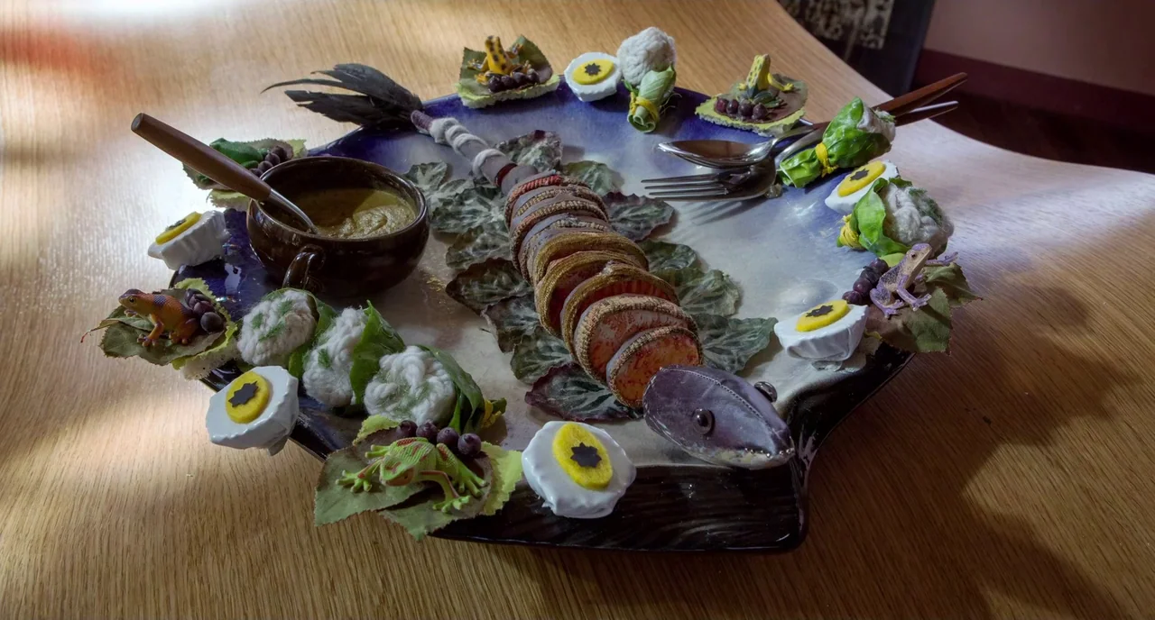 Mood Indigo (2013) movie still: closeup — A dark ceramic platter decorated with sculpted lizards, leafy greens, and boiled egg slices. The platter…