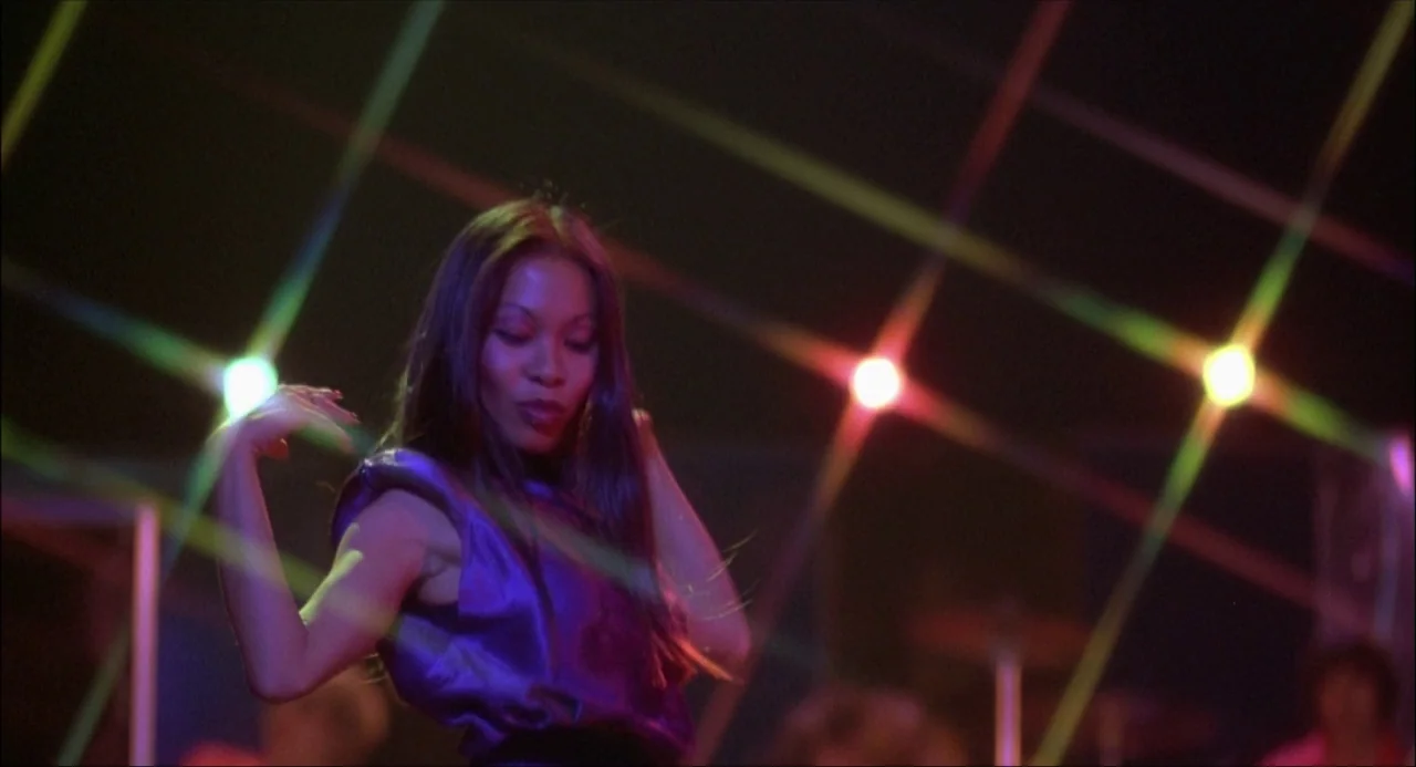 Xanadu (1980) movie still: medium — A dark venue filled with bright, multi-colored neon light beams crossing in the air. A woman dances in the…