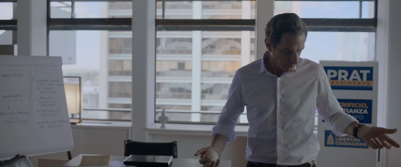 Doublespeak (2021) movie still: medium — A modern office space with large windows overlooking a city skyline. A man in a white shirt stands in front…