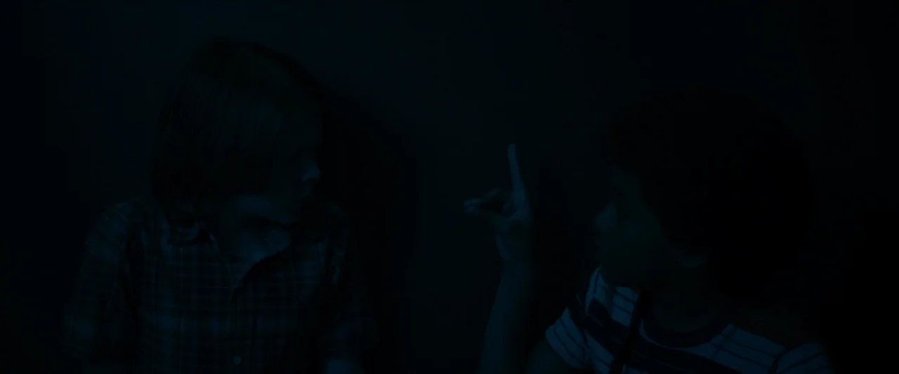 Wonderstruck (2017) movie still: medium — Two children face each other in a room submerged in near darkness. A boy raises his index finger while…