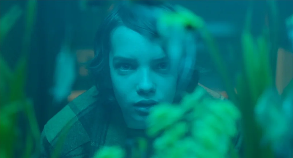The Congress (2013) movie still: closeup — A teenage boy looks through the glass of an aquarium filled with aquatic plants. The scene is bathed in…