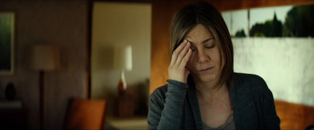 Cake (2014) movie still: medium — A dimly lit room with mid-century modern furniture and a framed wall art piece. A woman with shoulder-length brown…