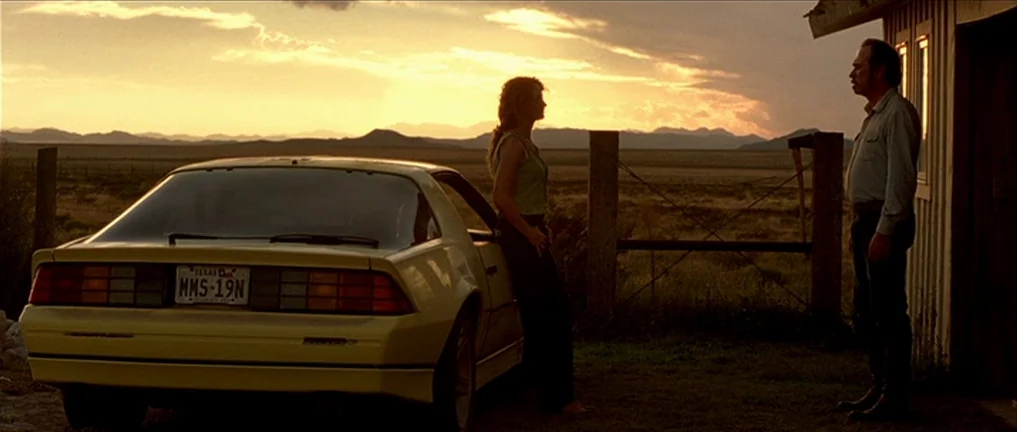 The Three Burials of Melquiades Estrada (2005) movie still: wide — An arid, flat landscape extends to distant mountains under a cloudy, golden…