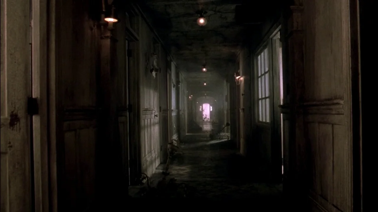 In Dreams (1999) movie still: wide — A dark, dilapidated hotel hallway with wood-paneled walls and a series of closed doors. Dim lights create deep…