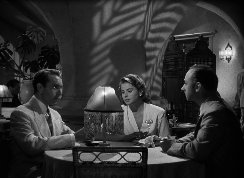 Casablanca (1942) movie still: medium — An interior space with arched ceilings and decorative room dividers creates a dark atmosphere. Three people…