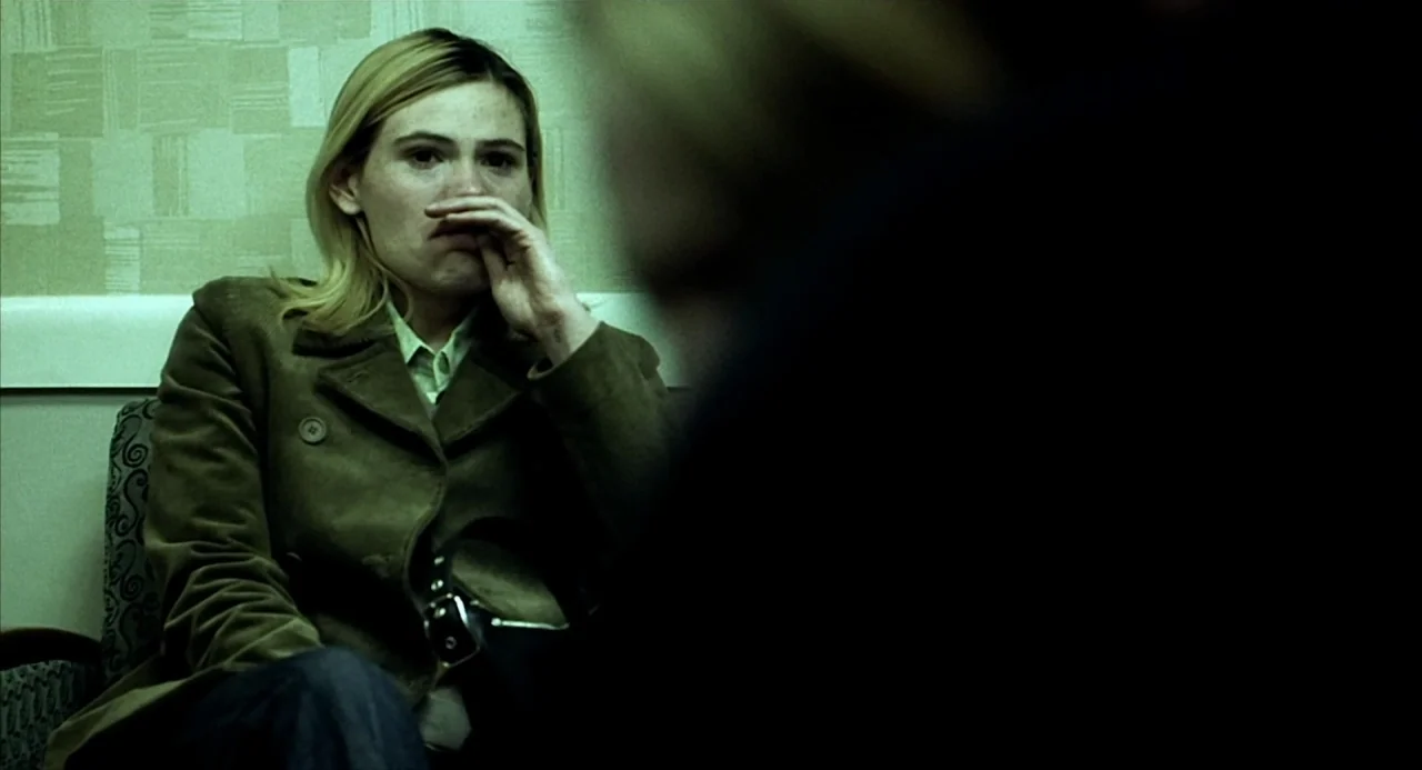 21 Grams (2003) movie still: medium — A waiting room with patterned green wallpaper and chairs upholstered in patterned fabric. A woman sits in a…
