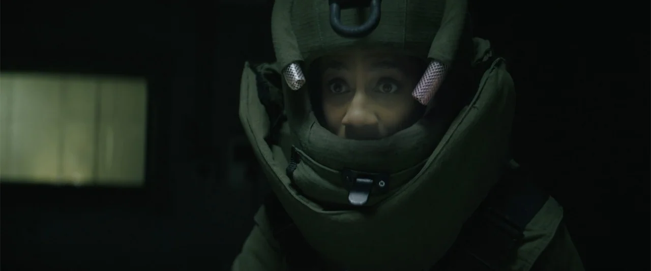 One Ranger (2023) movie still: closeup — A person is wearing a heavy olive green protective bomb disposal suit. The individual looks directly ahead…