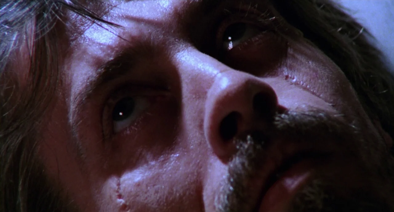 Caravaggio (1986) movie still: closeup — A close-up view of a man lying on a surface in a dark room. The man looks directly upward while his face is…