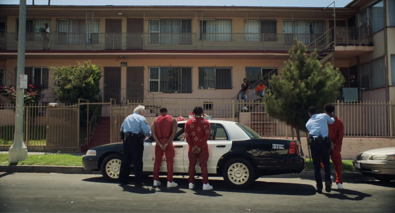 House Party (1990) movie still: wide — A two-story stucco apartment building features metal window grilles and outdoor staircases. Two police…