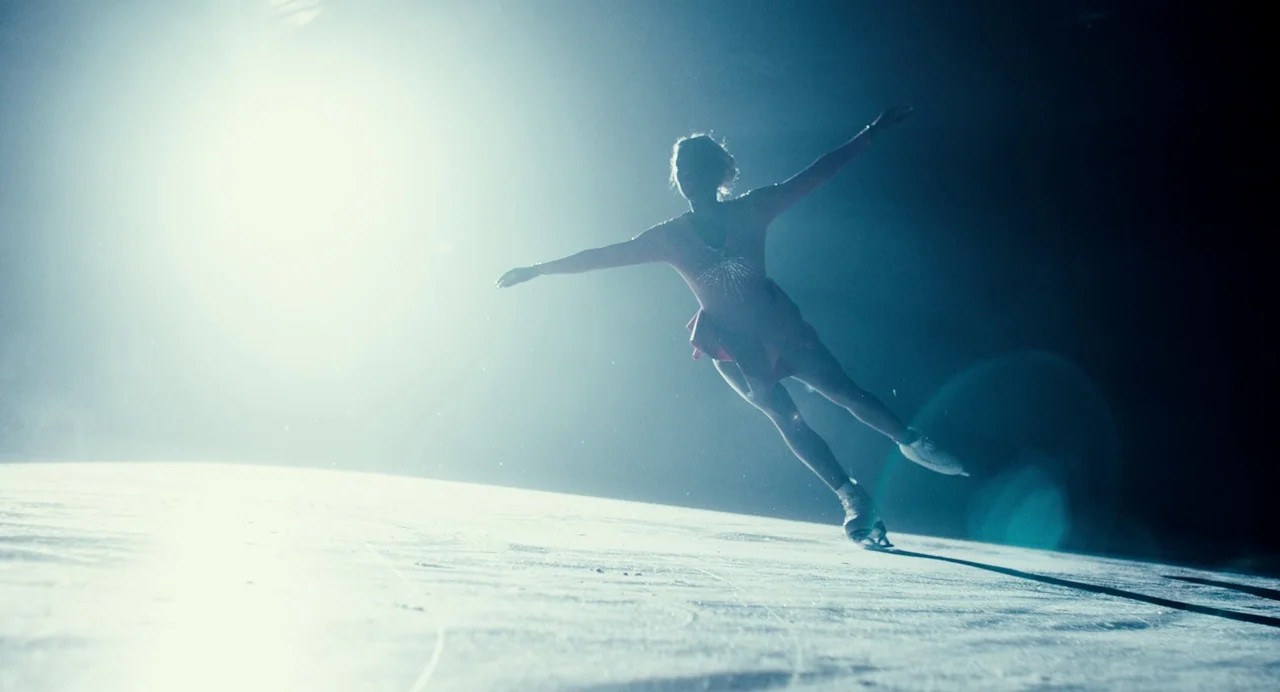 My Animal (2023) movie still: fullbody — An ice rink surface illuminated by a bright directional light source from the side. A figure skater in a…
