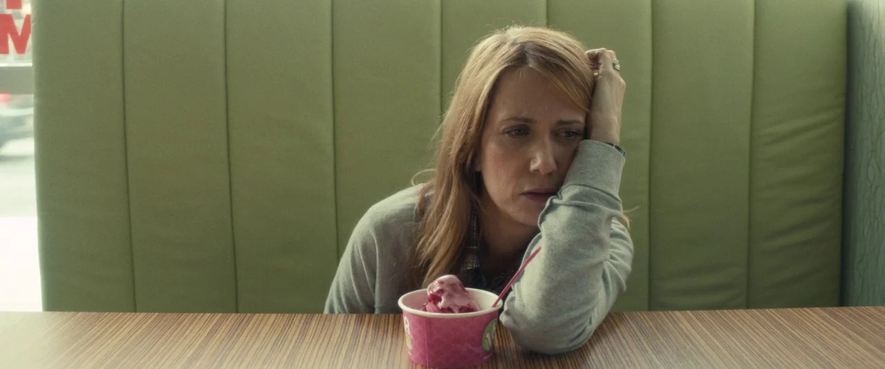 The Skeleton Twins (2014) movie still: medium — A woman sits in a green upholstered booth inside a bright, clean diner. She rests her chin on her…