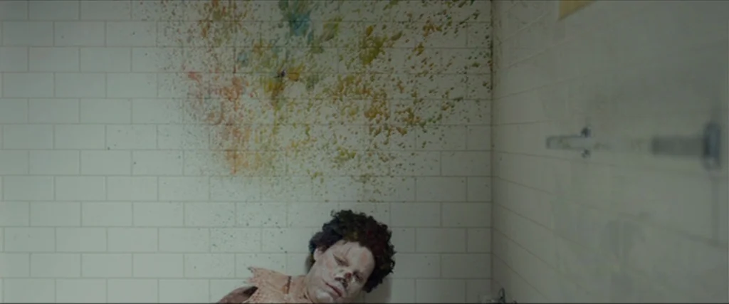 Clown (2014) movie still: medium — A sterile white tiled corner of a room features colorful paint splatters on walls. A person with white clown-like…