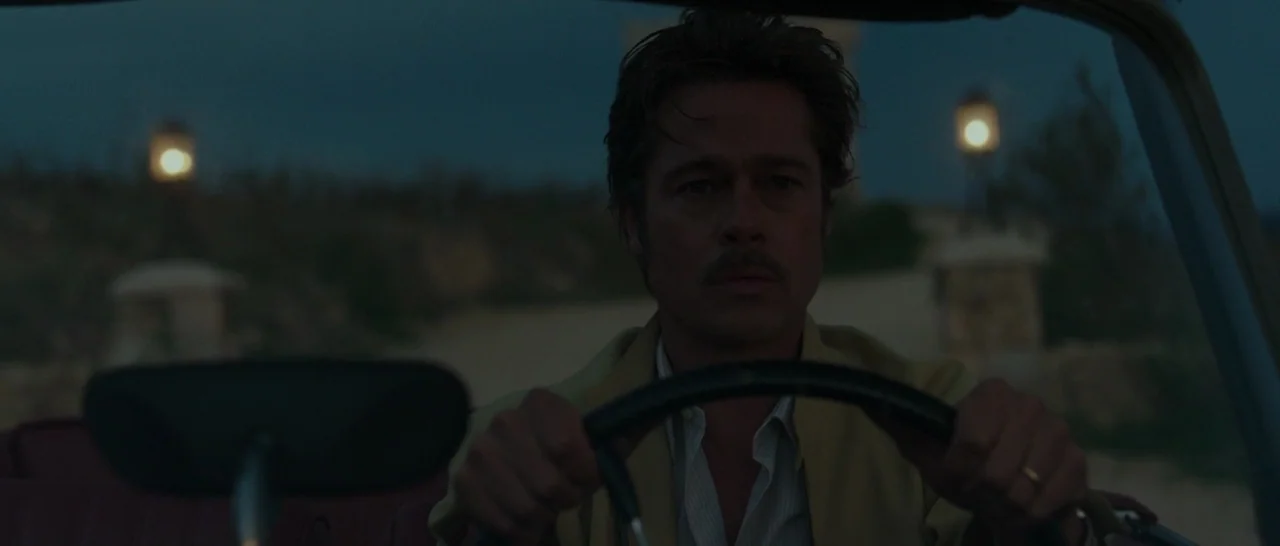 By The Sea (2015) movie still: medium — A man drives a vintage car through a dark landscape at night. Two glowing streetlamps stand in the distance…