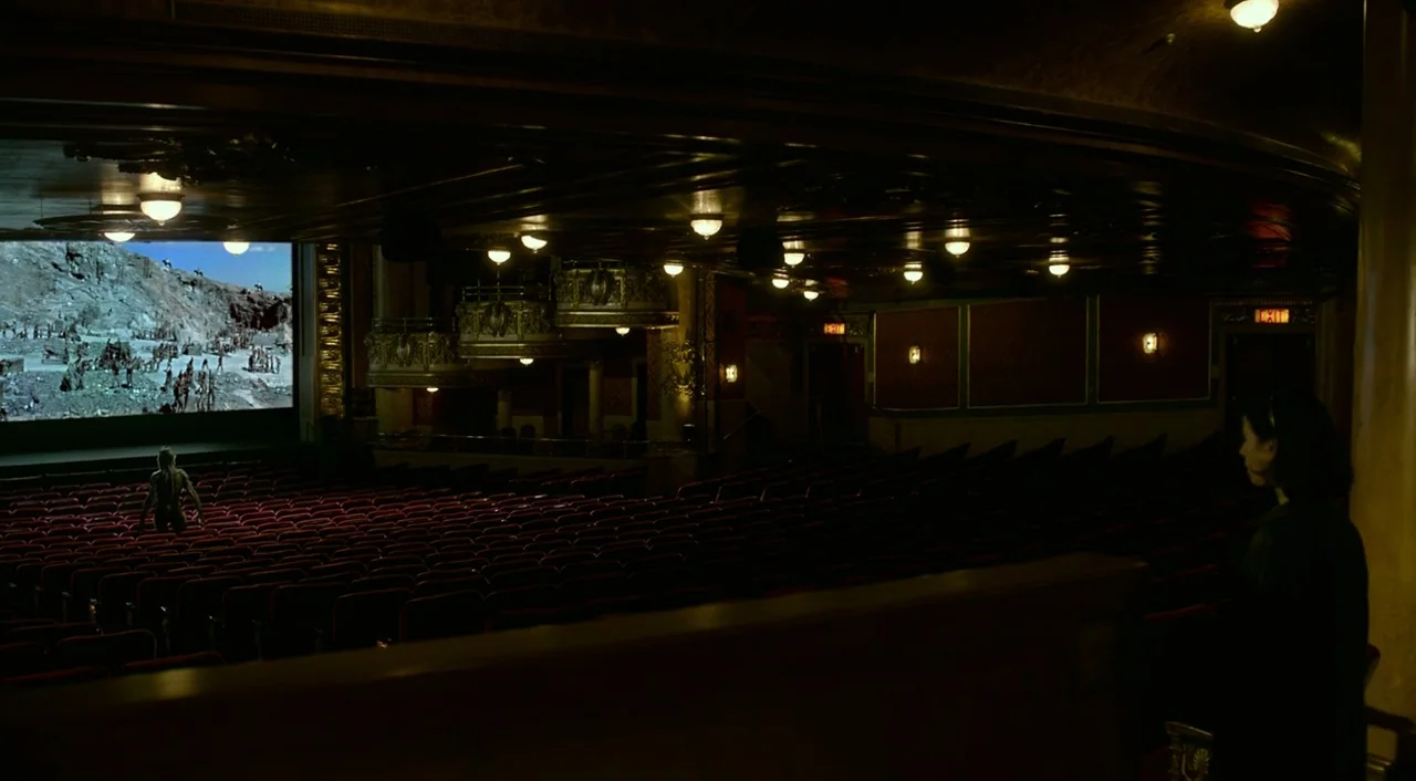 The Shape of Water (2017) movie still: wide — A dark, ornate movie theater interior features rows of empty red seats. A person stands alone in the…