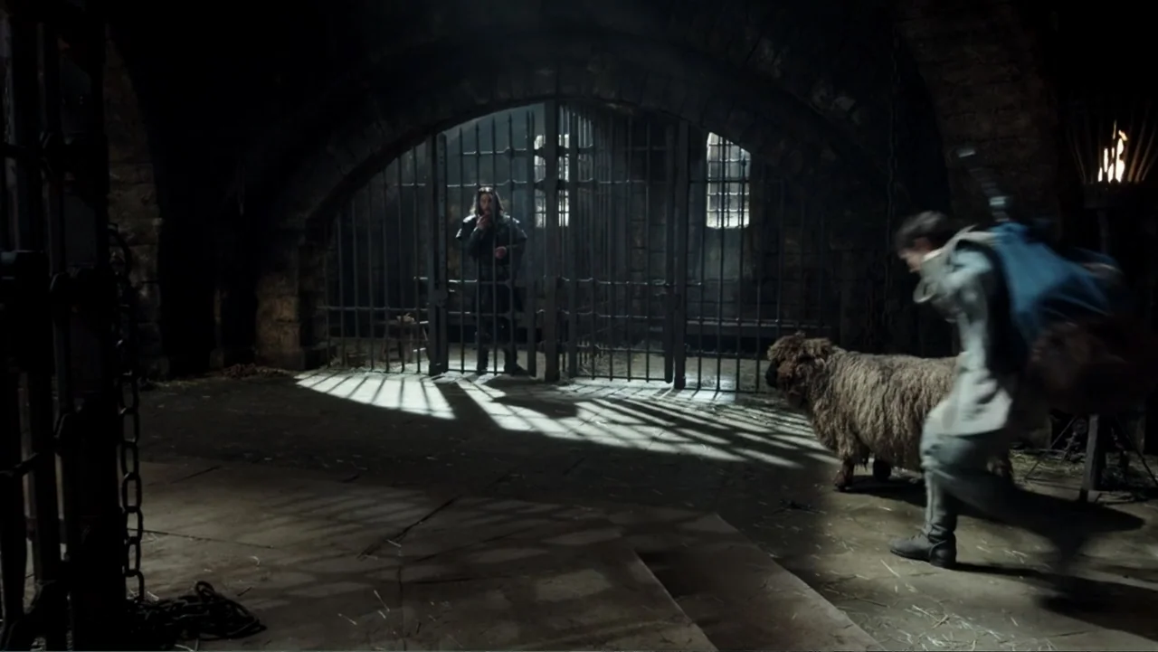 Warcraft (2016) movie still: wide — A dark stone dungeon features thick iron bars and a small window for light. A prisoner stands behind the gate…