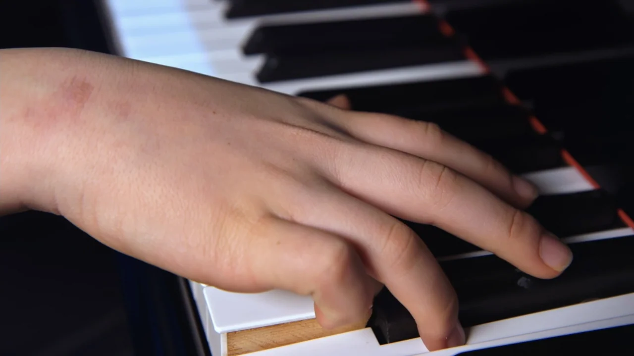 Moonlight Sonata: Deafness in Three Movements (2019) movie still: closeup — A close-up view shows a hand resting on a set of piano keys. Fingers are…