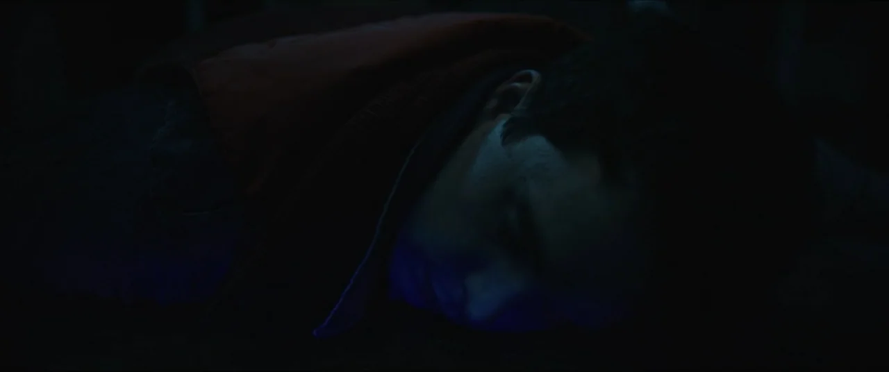 Vicious Fun (2021) movie still: closeup — A dark, dimly lit bedroom at night with minimal ambient light. A teenage boy with dark hair lies face down…