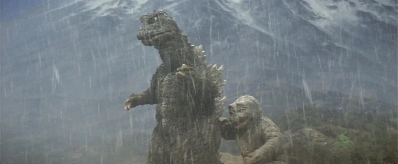Destroy All Monsters (1968) movie still: wide — A rain-swept mountainous slope features a large reptilian creature standing next to a smaller one.…