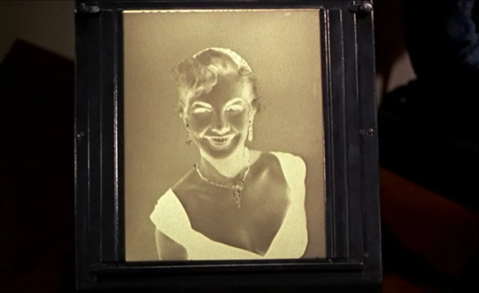 Rear Window (1954) movie still: closeup — A photographic negative plate is held in a dark room. The negative displays the portrait of a woman in a…