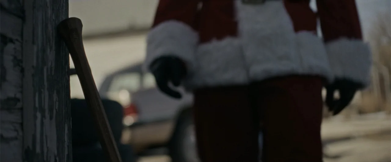 Silent Night, Deadly Night (2025) movie still: medium — An outdoor suburban area features a wooden post in the foreground and a parked car. A person…