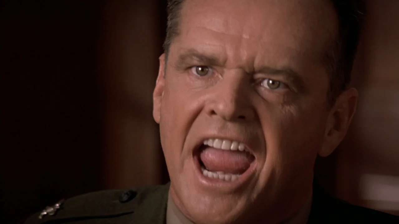 A Few Good Men (1992) movie still: closeup — An interior shot of a formal setting with dark, blurred wooden background details. A man in a military…