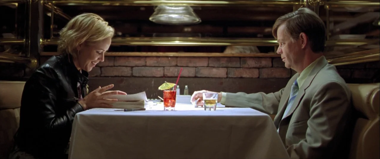 The Cooler (2003) movie still: medium — A booth in a dimly lit diner with a brick wall behind the table. A man and a woman sit facing each other…