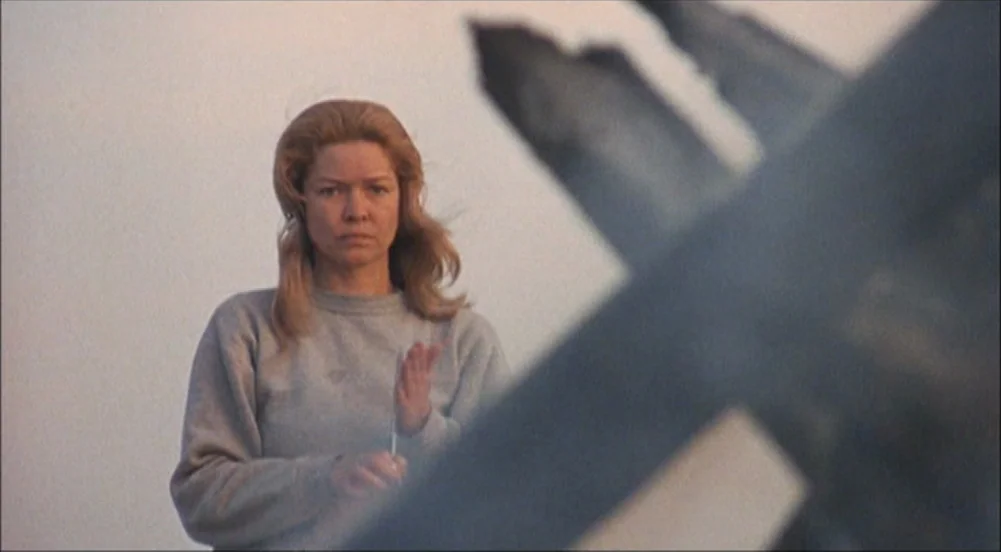 The King Of Marvin Gardens movie still: medium — A woman stands before a large, blurry metal structure on a sandy expanse. She holds a thin metallic…