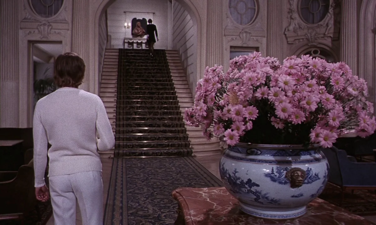 Daughters of Darkness (1971) movie still: medium — A grand, high-ceilinged hotel lobby features a wide staircase with an ornate runner rug. A man…