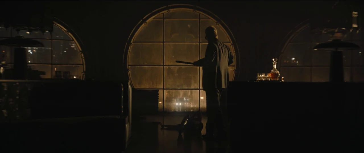 The Batman (2022) movie still: wide — A dimly lit lounge featuring dark booths and large, circular glass windows looking outside. A man in a suit…