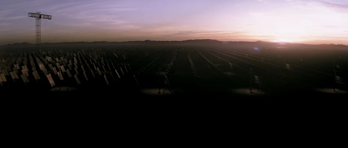 Transcendence (2014) movie still: establishing — A vast solar power facility features endless rows of tilted mirrors at daybreak. A tall steel…
