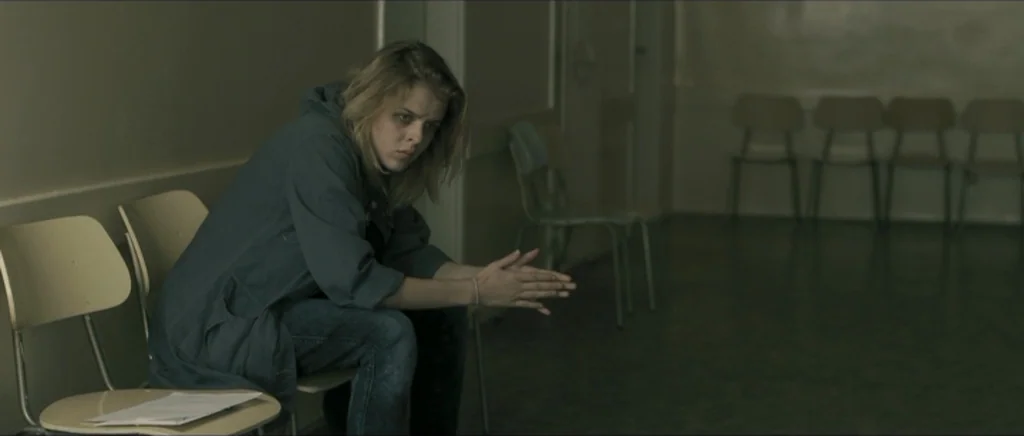 Lasting (Nieulotne) (2013) movie still: medium — A sparsely furnished, sterile waiting area features rows of identical metal chairs. A young woman…