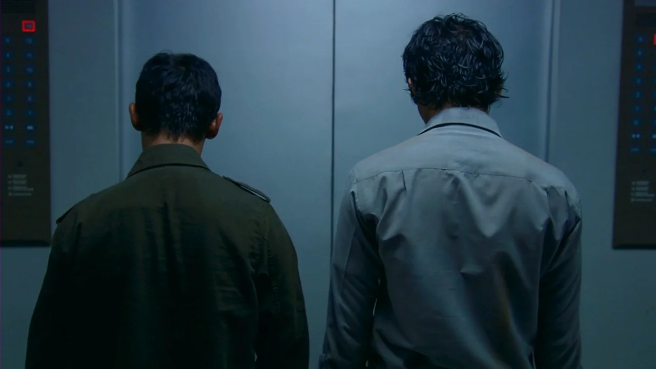 Merantau (2009) movie still: medium — A metal-paneled elevator car with illuminated floor selector buttons on both side walls. Two men stand with…
