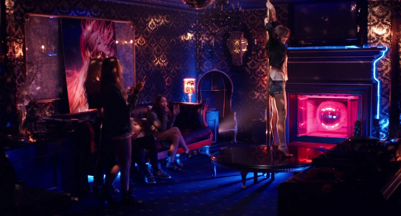 The Bling Ring (2013) movie still: wide — A dark, opulent room features patterned wallpaper, a fireplace, and a dance pole. A woman dances on the…