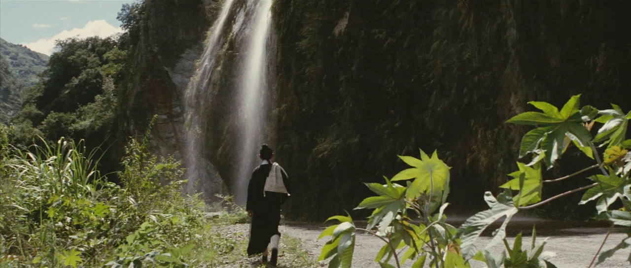 A Touch of Zen (1971) movie still: fullbody — A narrow dirt trail runs alongside a tall waterfall surrounded by lush, dense vegetation. A solitary…