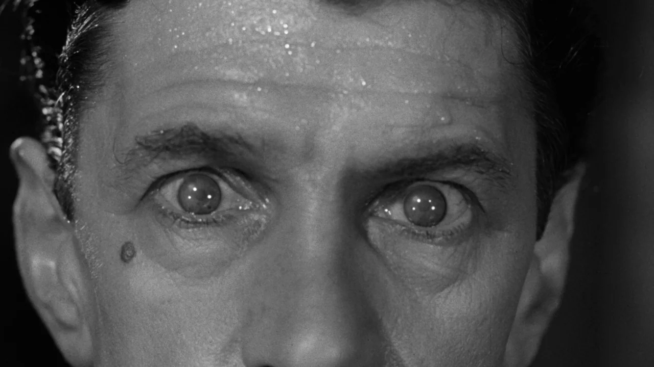 Village of the Damned (1960) movie still: closeup — A tight closeup shot focuses exclusively on a man's face and eyes. He is perspiring and staring…