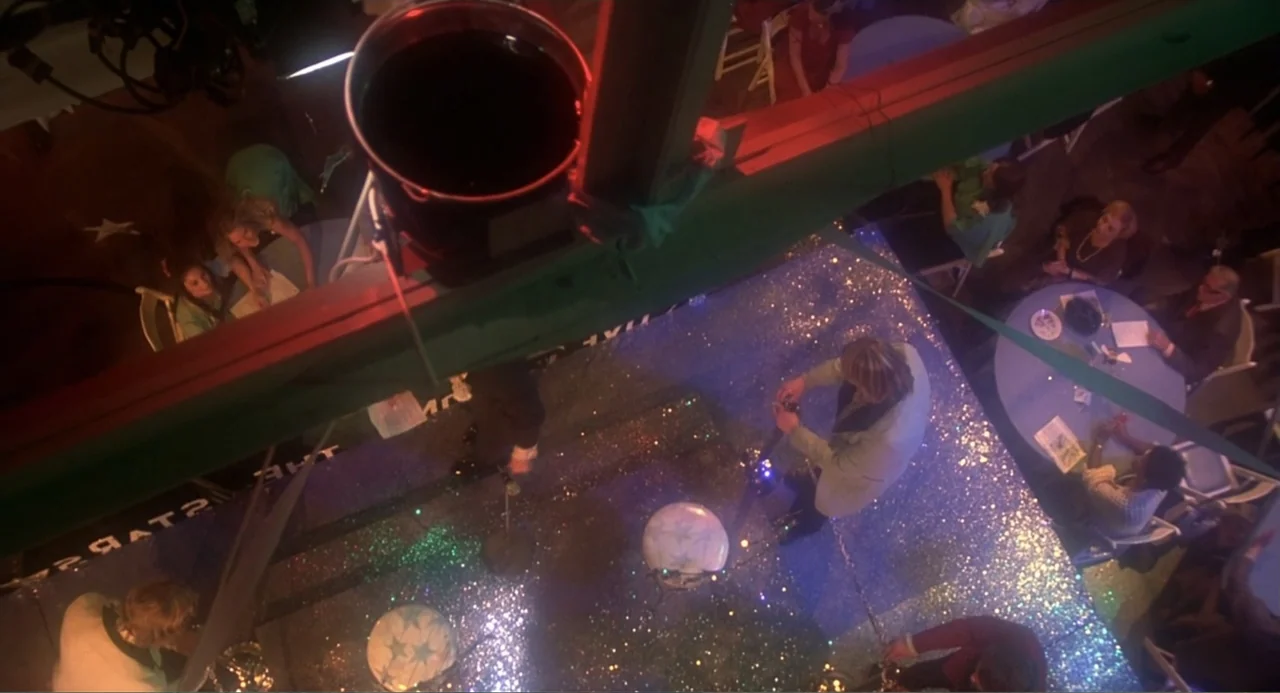 Carrie (1976) movie still: wide — A nightclub floor covered in reflective glitter illuminated by rotating colored stage lights. A musician stands on…