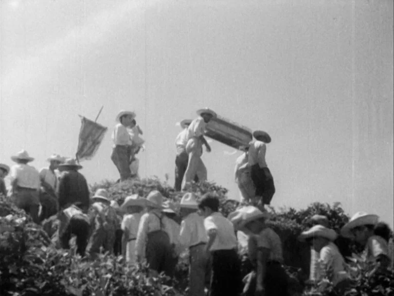 Redes (1936) movie still: wide — A crowd of people wearing hats walks up a grassy, sunlit hillside. Several men near the center of the frame carry a…