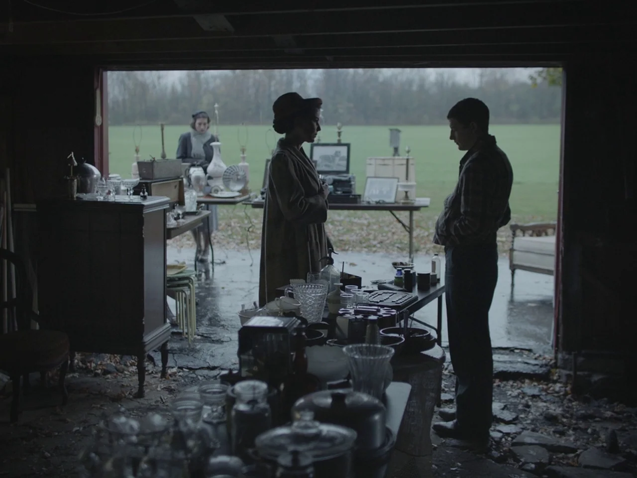 The Mountain (2018) movie still: fullbody — An open suburban garage is filled with miscellaneous household items organized on folding tables. A man…