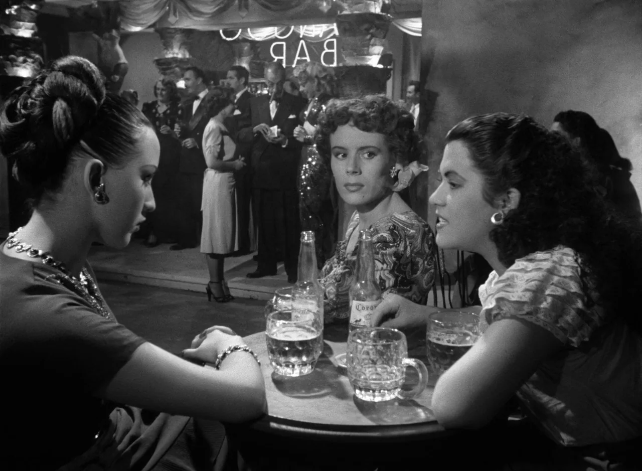 Victims of Sin (1951) movie still: medium — A crowded 1940s nightclub interior with blurred patrons moving in the background. Three young women sit…
