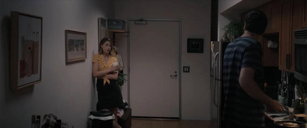 Equation of Love and Tone Deafness (2015) movie still: medium — An apartment interior features a hallway with framed art and a small kitchen area. A…