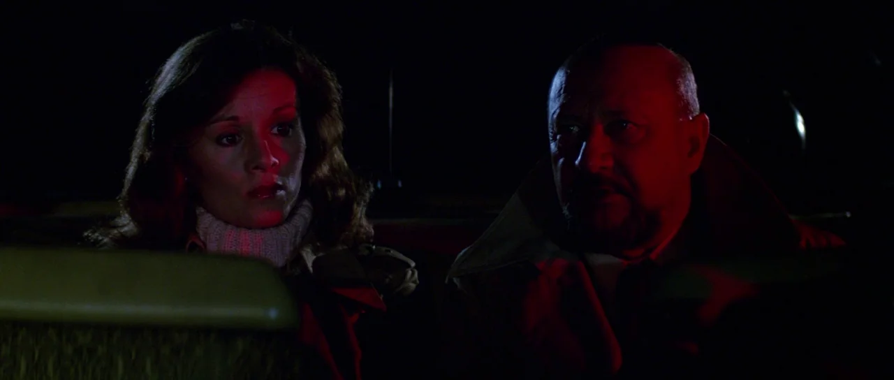 Halloween II (1981) movie still: medium — The interior of a vehicle at night is dark with minimal ambient light. A man and woman sit side by side in…
